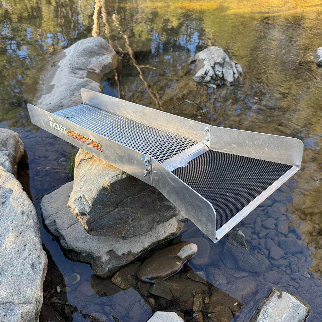 Aluminium sluice with a picket prospecting logo on the side, displaying v matting on the top in a creek setting.