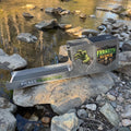 A metal prospecting sluice box with a slotted trough, placed on rocks beside a rocky stream. The side of the box shows a green claw graphic and the text 'FRANKEN SLUICE,' and the trough has 'PICKET PROSPECTING' printed on it.