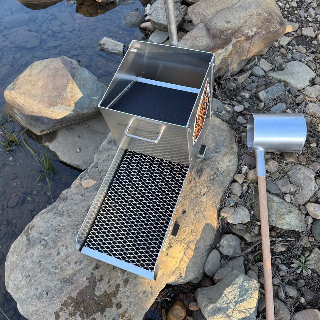 Aluminium rocker box placed on a large rock in a creek setting. Displaying expanded mesh and a classifying sieve.